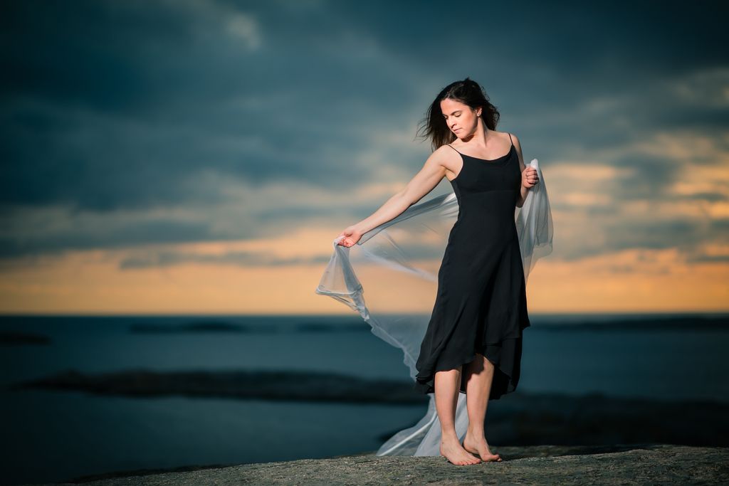Dramatic environmental fashion portrait at sunset coast featuring woman in elegant black dress