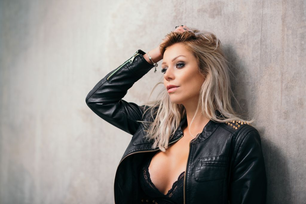 Moody fashion portrait photography featuring blonde woman in leather jacket against concrete wall